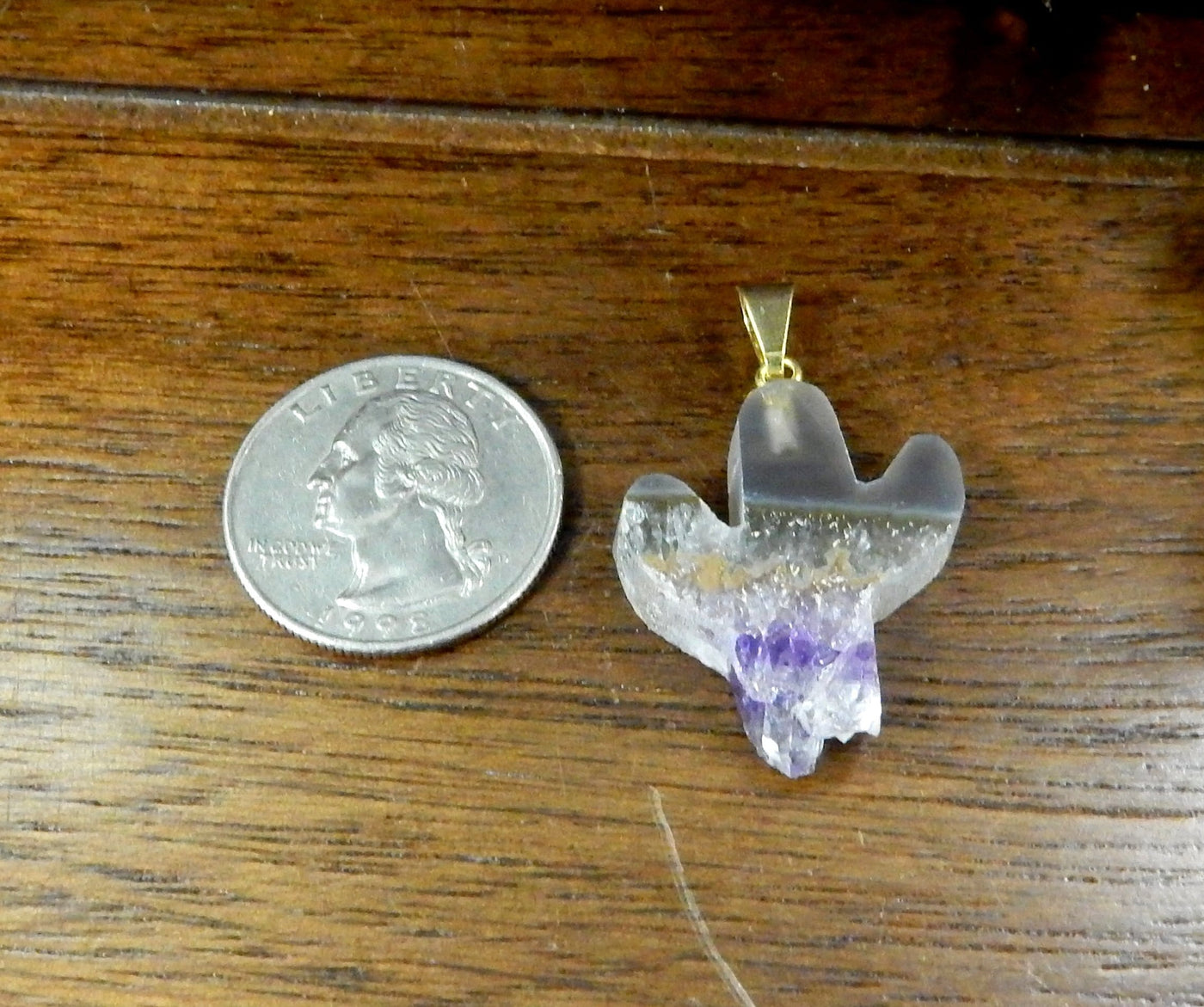 amethyst slice cactus pendant next to a quarter on wooden background
