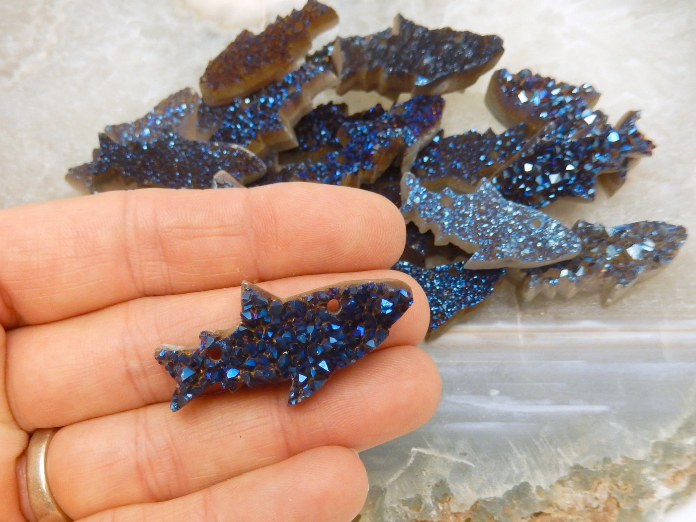 hand holding up Mystic Blue Shark Fish Cluster Cabochon with others in the background