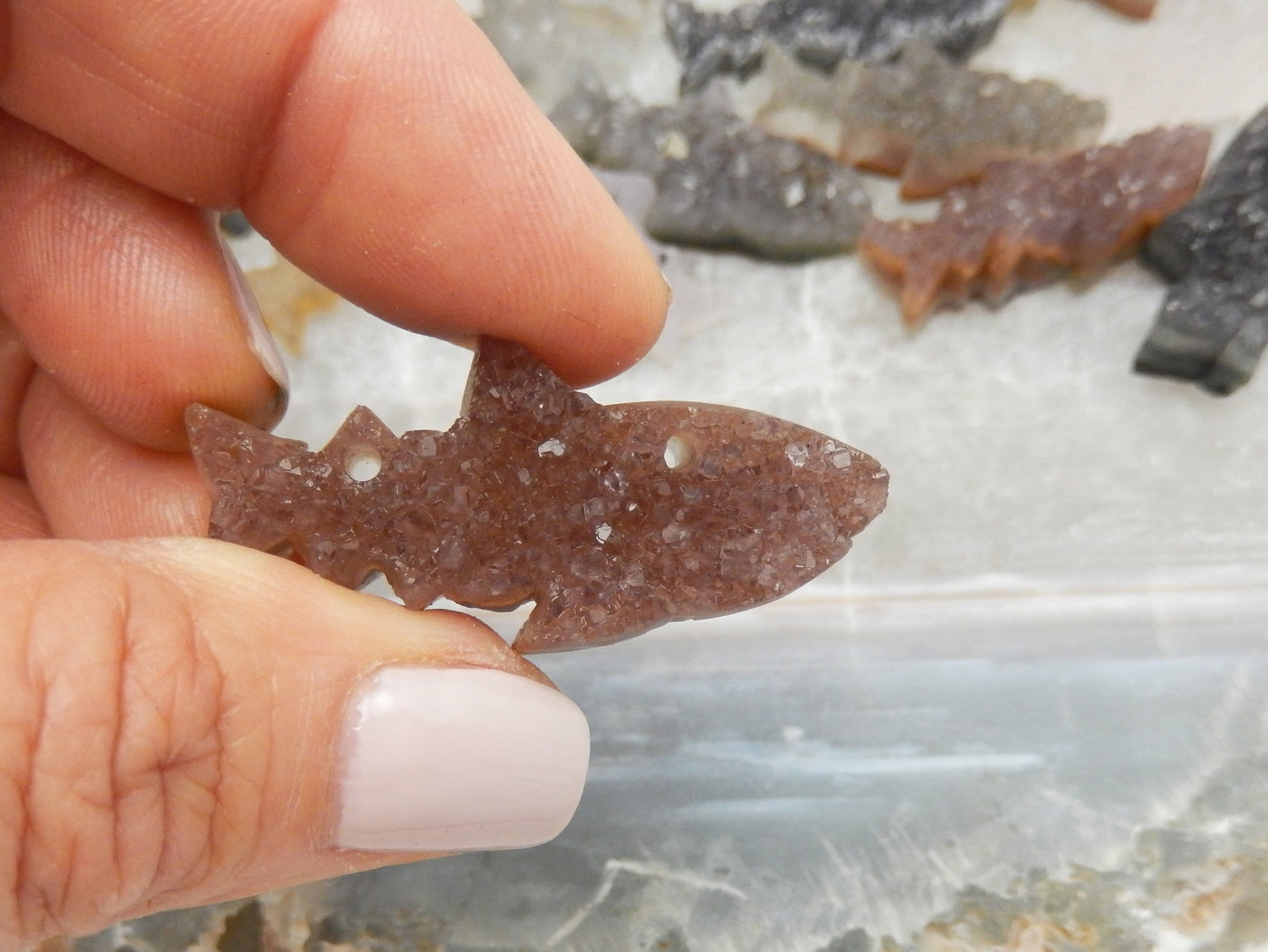 Fingers holding one orange Druzy Shark Fish Cluster Cabachon for size reference 