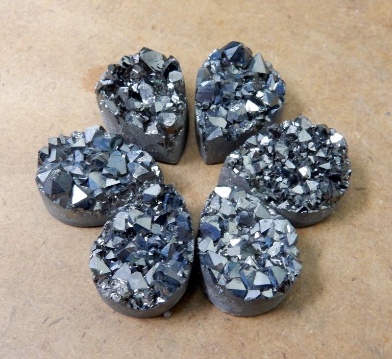 Multiple Platinum Titanium Druzy Teardrop Cabochons displayed on brown background to show various textures and overall characteristics 