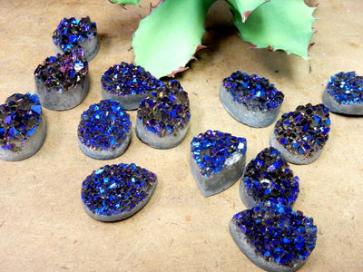 Multiple Mystic Blue Titanium Druzy Teardrop Cabochons displayed on brown background to show various textures and overall characteristics 