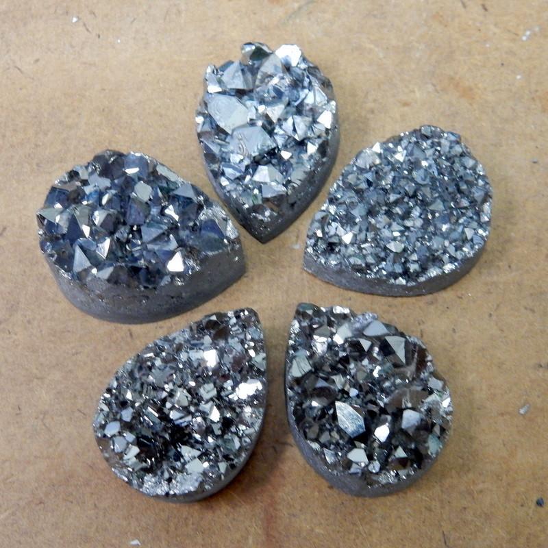 Multiple Platinum Titanium Druzy Teardrop Cabochons displayed on brown background to show various textures thickness and overall characteristics 