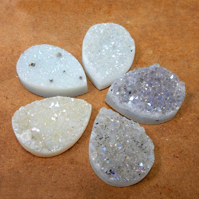 Multiple White Shimmer Titanium Druzy Teardrop Cabochons displayed on brown background to show various textures and overall characteristics 