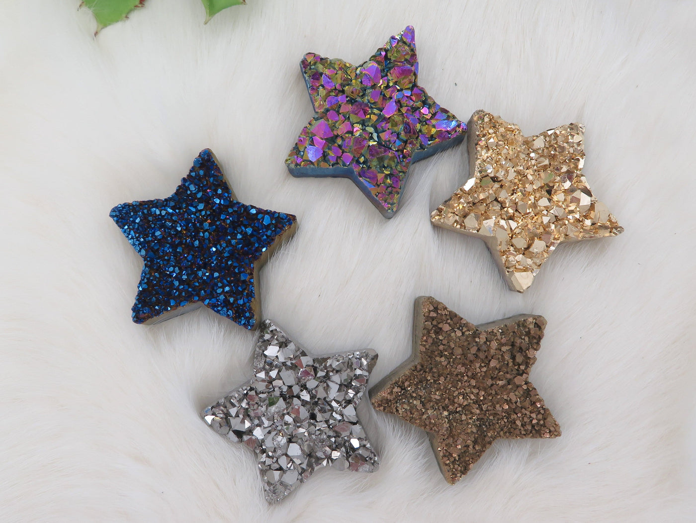 Five differently colored Titanium Treated Druzy Stars displayed on fuzzy surface.