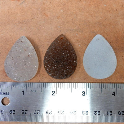 3 pieces of the Teardrop Druzy Cabochon Top Center Drilled next to a ruler for sizing , The measurement of these stones range from: 28mm x 40mm