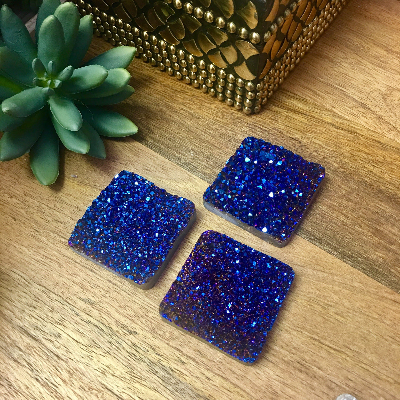 3 druzy diamond shaped beads on wooden table with plant in the background