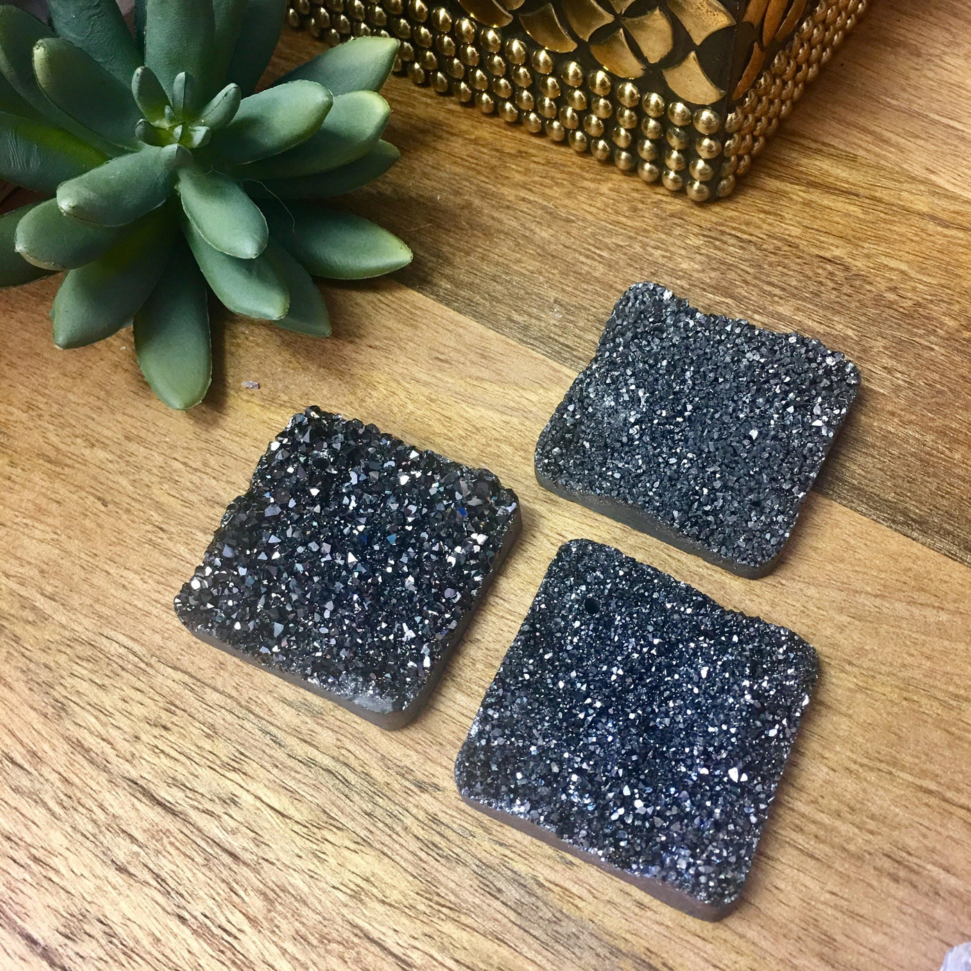 3 druzy diamond shaped beads on wooden table with plant in the background