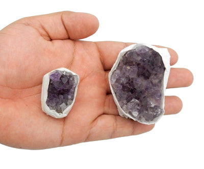 hand holding up 2 different sized amethyst clusters