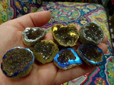 hand holding up 7 mystic half geodes in gold, platinum, and rainbow 