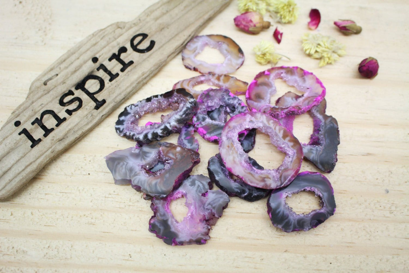 Multiple Dark Pink Geode Slice on Top Each other next to Inspire Wooden piece Sign and Flowers on the Side on Wood background.