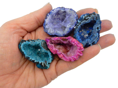 hand holding up teal, purple, pink, and blue dyed geode halves