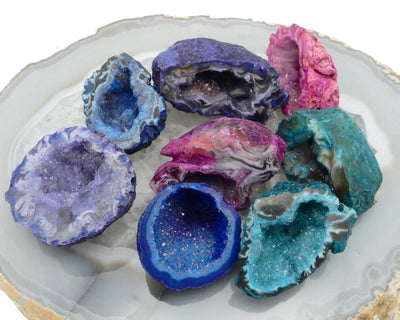 8 dyed geode halves in pink, purple, blue, and teal on agate slab
