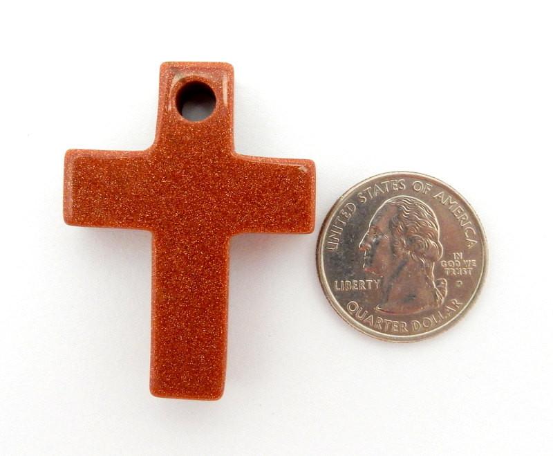 Goldstone red with sparkles cross on a white background.  It has a drilled hole on the top.  Placed next to a quarter to show it is bigger than the quarter.