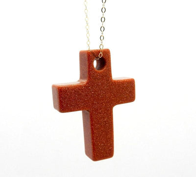 Goldstone red with sparkles cross on a white background.  It has a drilled hole on the top.  Hanging from a gold chain.