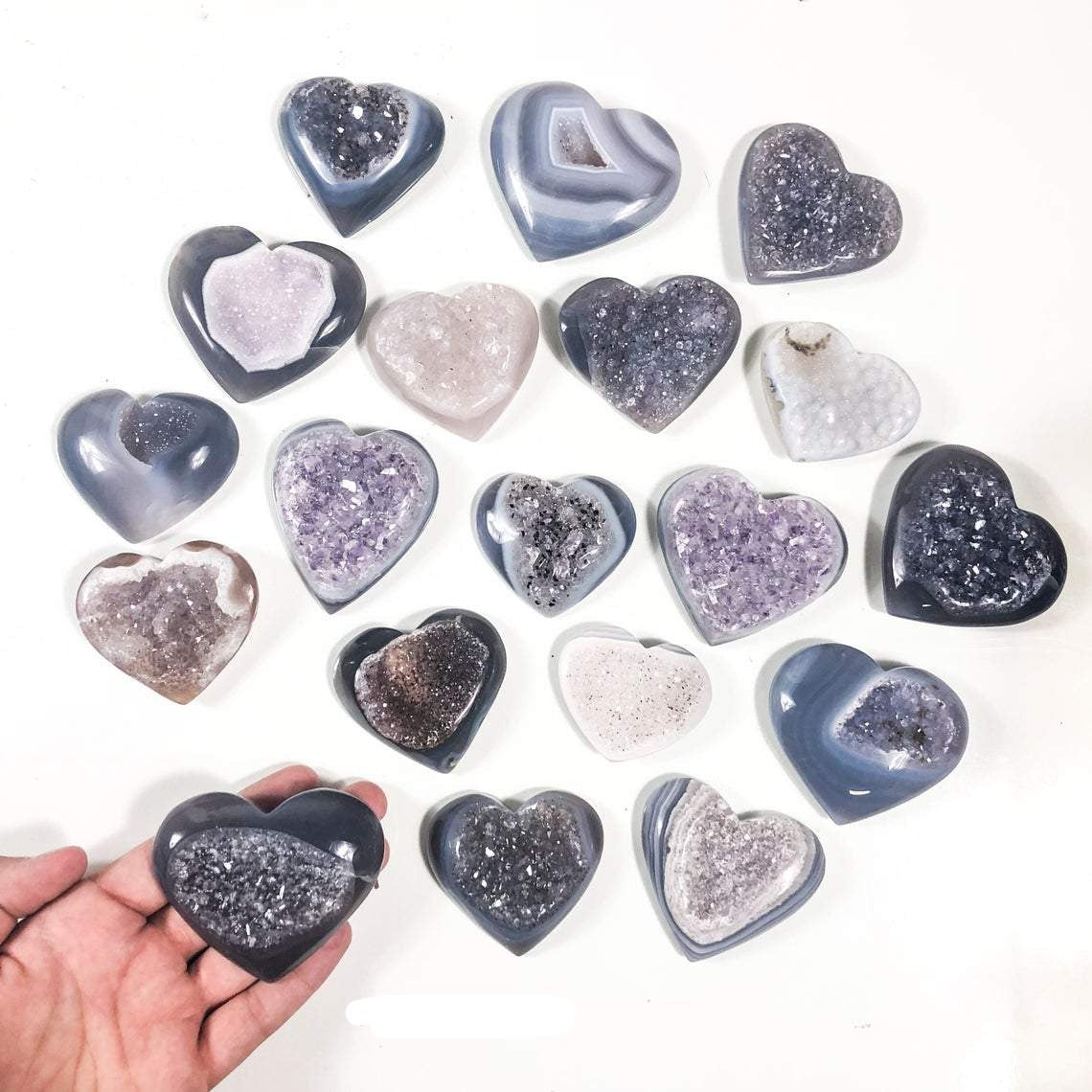 One agate druzy heart in a hand. Multiple agate druzy hearts on a white background displaying color and pattern variation.