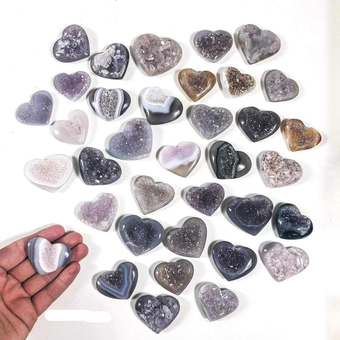 Agate Druzy Heart in a hand and multiple agate hearts shown on a white background to display color, pattern and size variation.