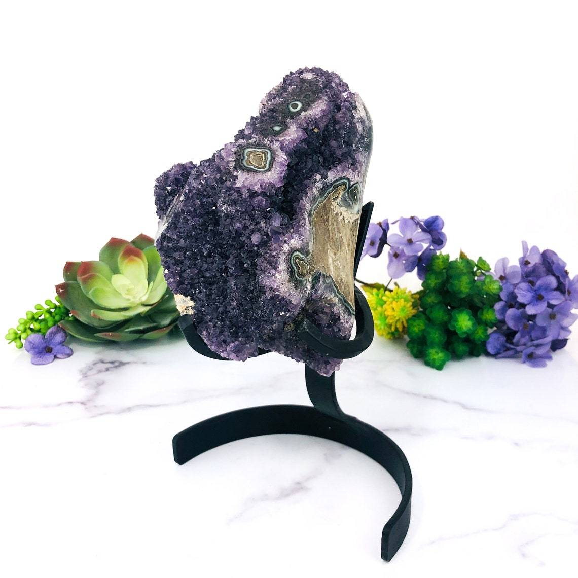 side view of Amethyst Purple Geode Crystal With Stalactite on Metal Stand with decorations in the background