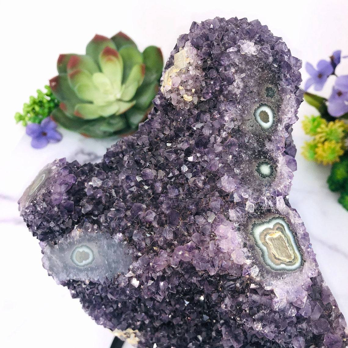 up close shot of Amethyst Purple Geode Crystal With Stalactite on Metal Stand with decorations in the background