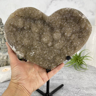 hand next to Druzy Heart on Stand with decorations in the background