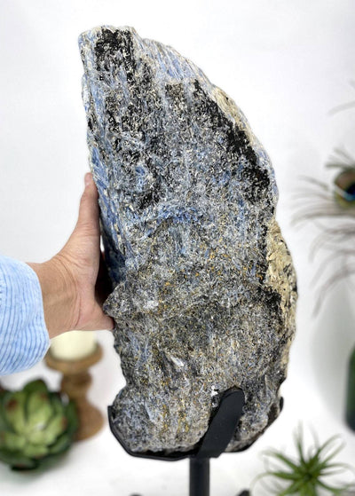 hand next to Products Blue Kyanite on Metal Stand with decorations in the background