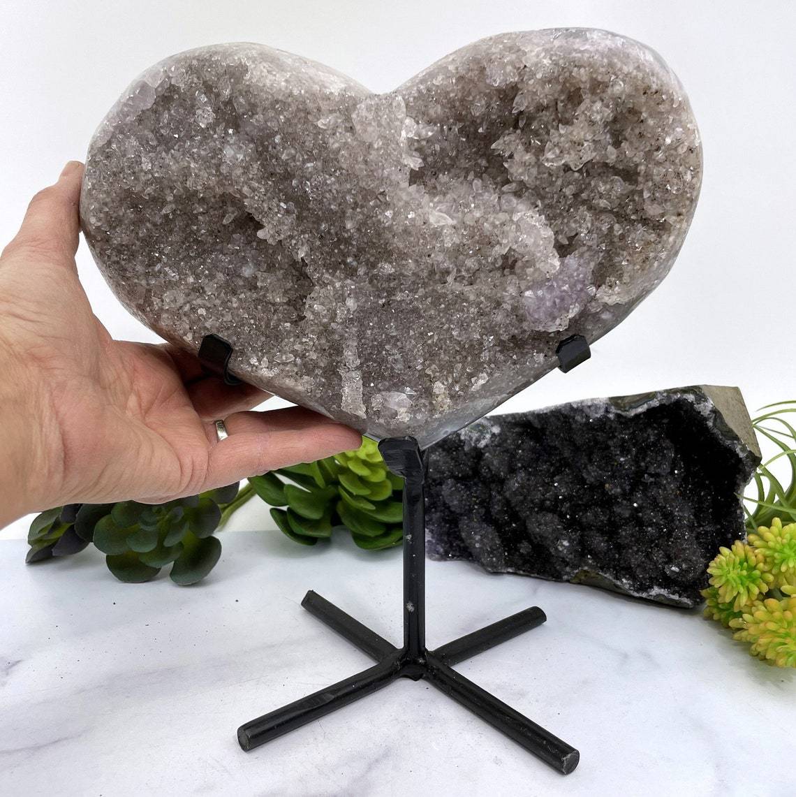 hand next to Amethyst Druzy Heart On Metal Stand with decorations in the background