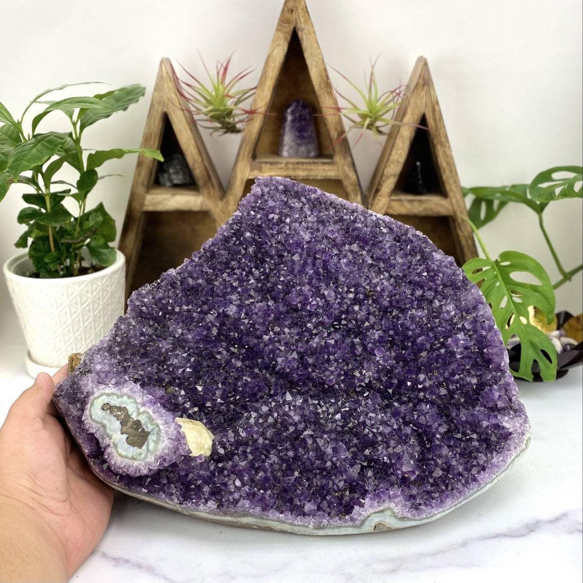 hand next to Amethyst Cluster with a Stalactite with Calcite with decorations in the background