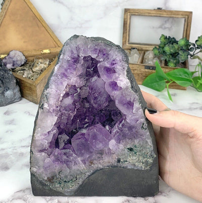 hand next to Amethyst Geode Cathedral with decorations in the background