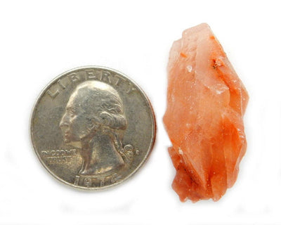 Red Calcite Stone next to quarter for size reference on white background