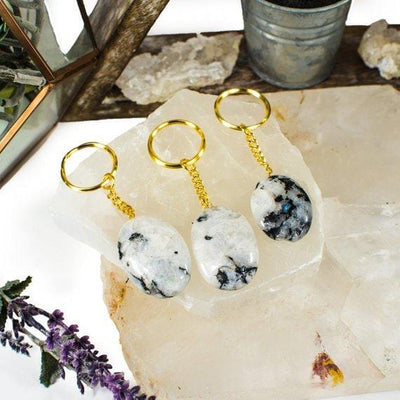 3 Rainbow Moonstone Worry stone Keychains on crystal quartz slab with various decorations in the background