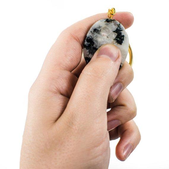 Hand holding Rainbow Moonstone Worry stone Keychain with thumb demonstrating how to use it