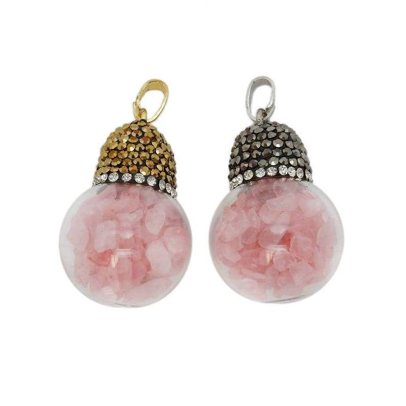 Two glass ball pendants filled with rose quartz chips on a white background.  One has a gold top with rhinestones, the other one has a dark silver top with rhinestones.