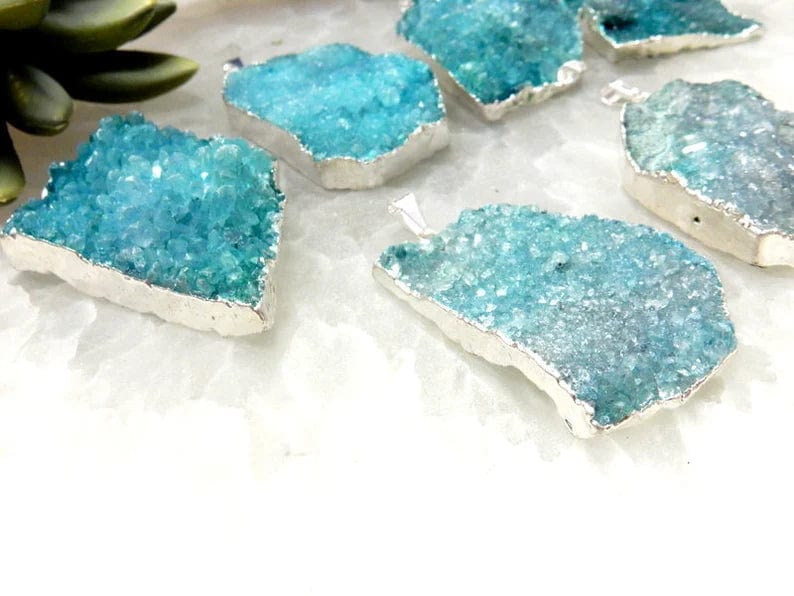 Side view of several teal druzy pendants showing the silver plating around the edges of them.