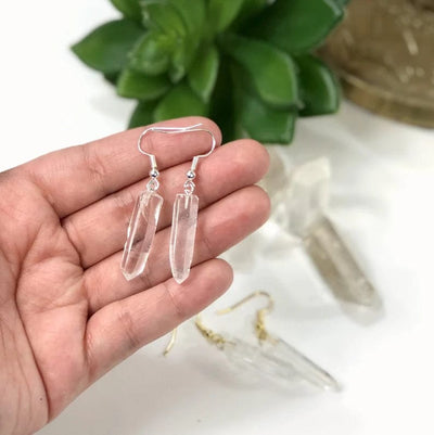 A pair of crystal point earrings with silver ear wires in a woman's hand.  Two more pairs are blurred in the background.