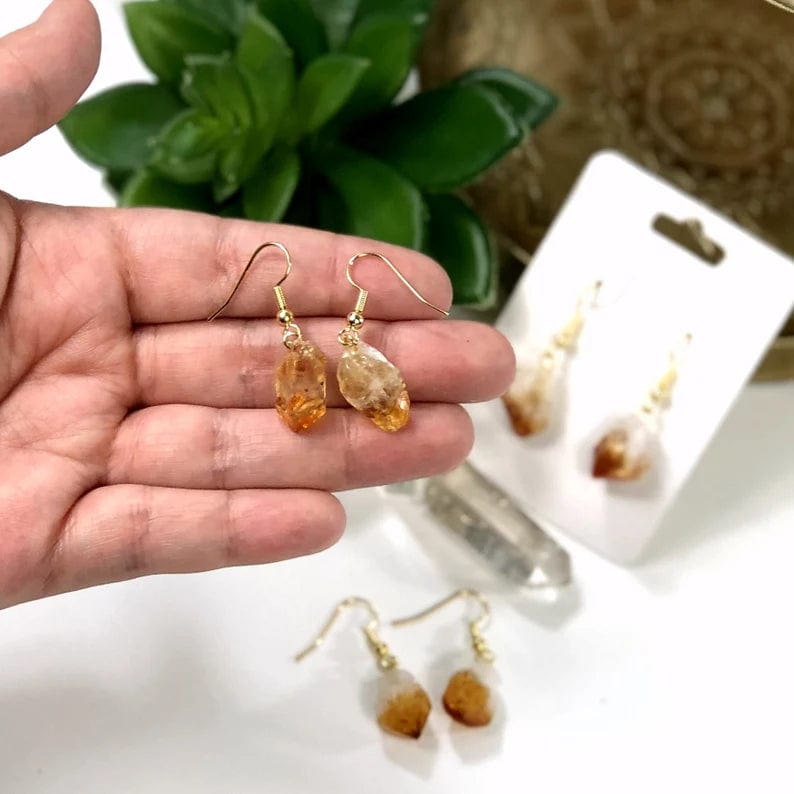 Citrine point earrings with gold plated ear wires in a woman's  hand.  Two more pairs are blurred in the background.