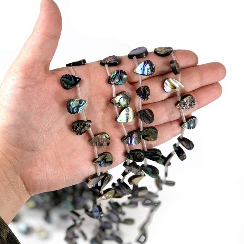 Multiple Abalone Drop Beads on a strand displayed on a hand. 