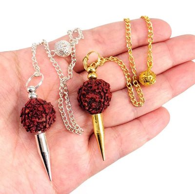 Two radruska pendulums in a woman's hand.  They have a brown radruska bead with a silver spike or a gold spike.