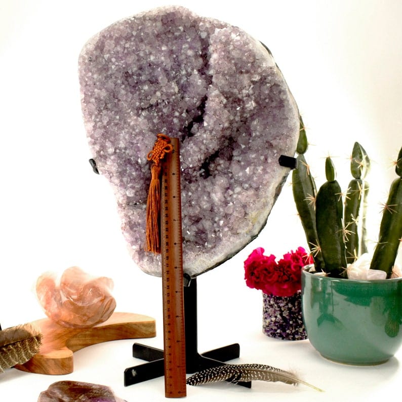 Large amethyst cluster on a black metal stand with a ruler only going a little more than half way up next to it.