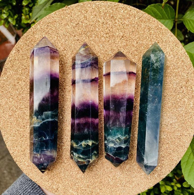 Top view of 4 Rainbow Fluorite Polish Double-Point Wands on corkboard with plants in the background