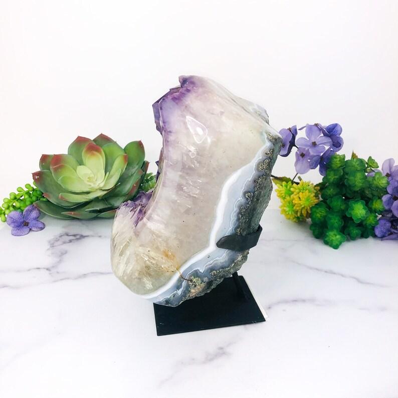 side view of Amethyst Purple Geode Crystal on Metal Stand  with decorations in the background