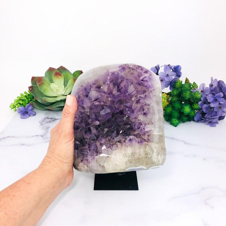 hand next to Amethyst Purple Geode Crystal on Metal Stand  with decorations in the background