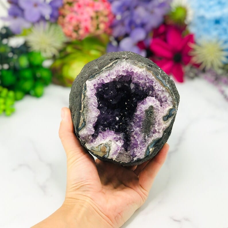 Round amethyst geode with a black outer shell in a woman's hand.