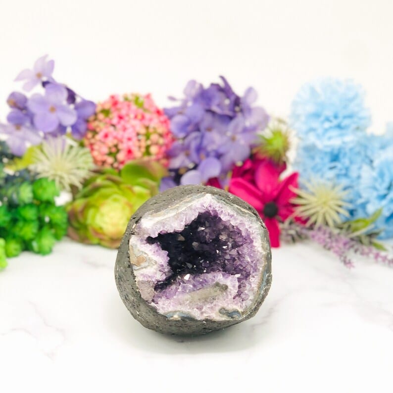 Round amethyst geode on a white background with flowers in the background.