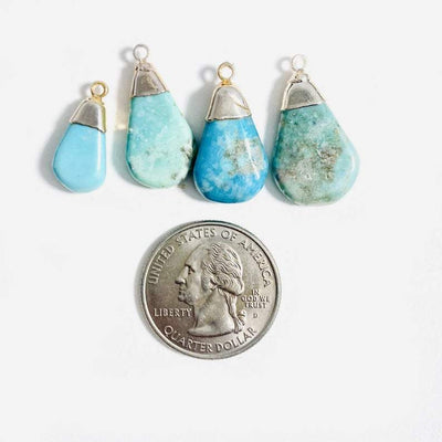 Silver plated natural turquoise teardrop pendants next to a quarter to show they are about the same size as a quarter.