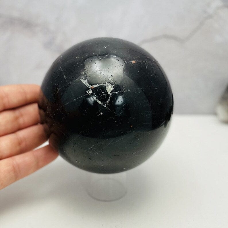 Black Tourmaline with Hematite Polished Sphere next to hand for size comparison