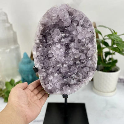 Amethyst cluster on a black metal stand next to a woman's hand.