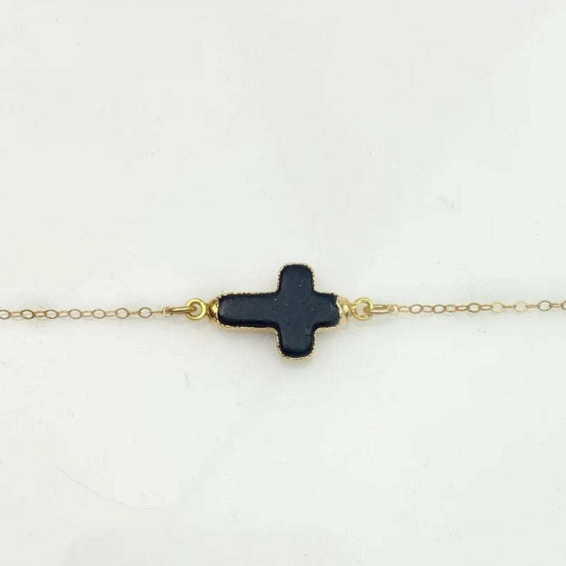 Black howlite sideways cross charm on a gold fill chain on a white background.