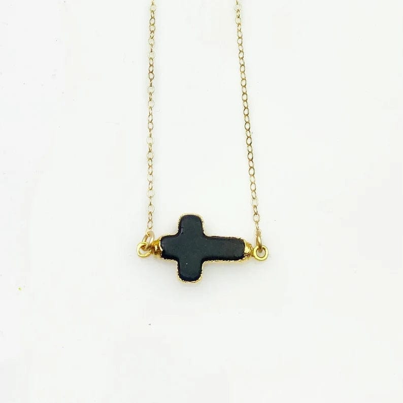 Black howlite sideways cross charm on a gold fill chain on a white background.