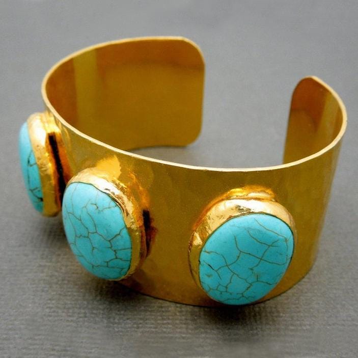 One gold plated cuff bracelet with three turquoise howlite stones on a gray background.
