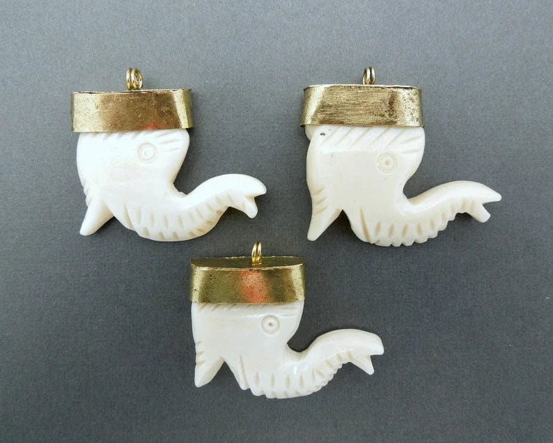 3 carved bone pendants with brass caps on a grey background