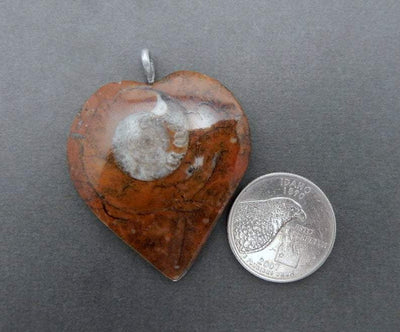 single heart shaped ammonite pendant with silver plated bail next to a quarter for size reference